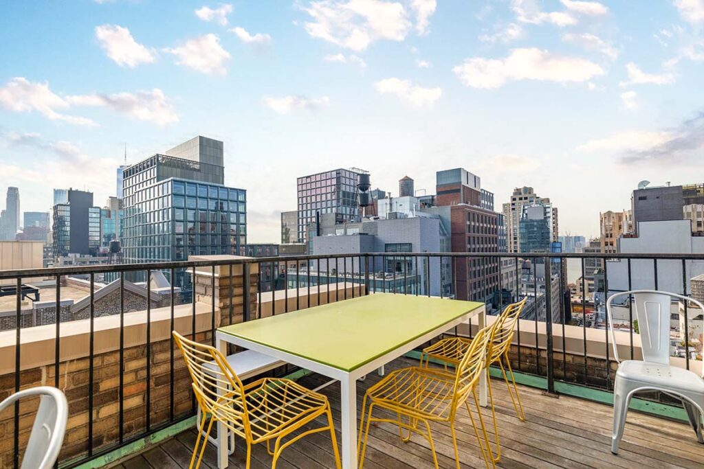 View from balcony of office overlooking other tall office buildings. In photo a green top table with yellow chairs. 